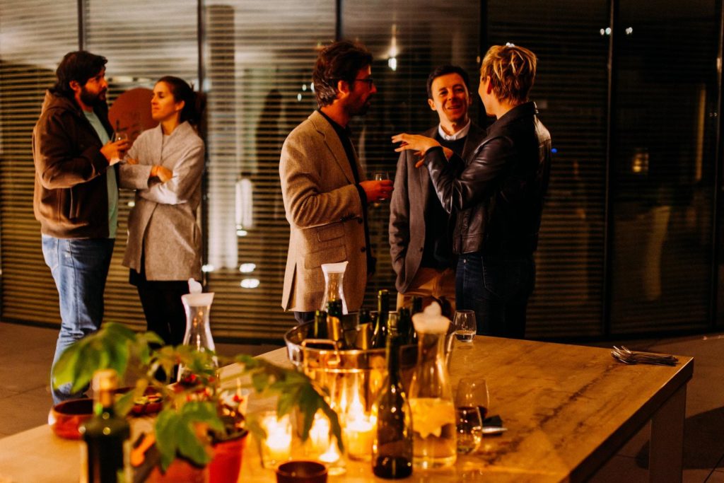 Five people in business casual attire converse in a candlelit office meeting room decorated for a party.